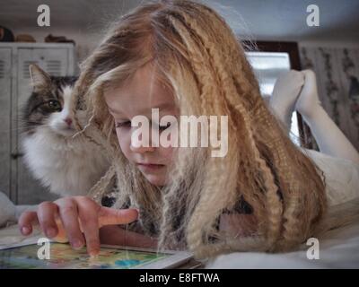 Ragazza che si stese a letto con il suo gatto utilizzando un tablet digitale, Svezia Foto Stock