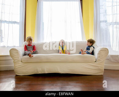 Tre bambini seduti su un divano nel soggiorno Foto Stock