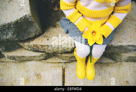 Ragazza seduta su un gradino che tiene un daffodil Foto Stock