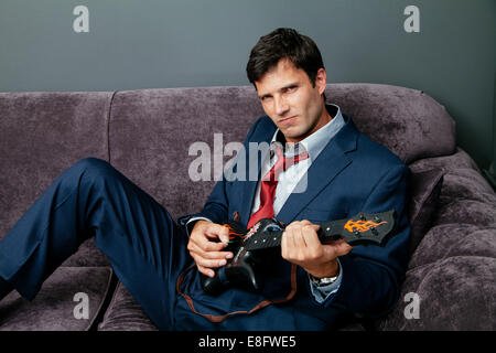 Uomo d'affari seduto su un divano che suona una chitarra giocattolo Foto Stock