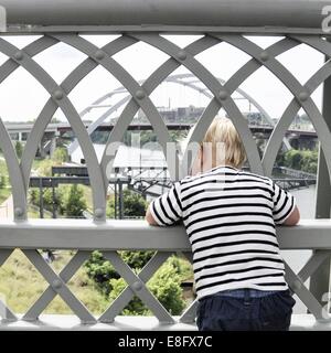 Ragazzo in piedi sul ponte guardando attraverso le ringhiere Foto Stock