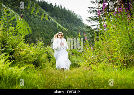 Una giovane donna bionda ragazza modello 'sposa indossa un bianco Palla abito abiti da sposa che corre lungo un percorso nel bosco estate REGNO UNITO Foto Stock