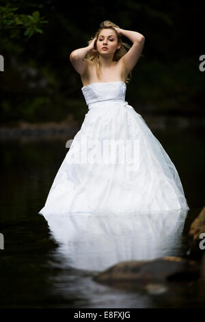 "Cestino il vestito": una giovane donna bionda ragazza modello sposa che indossa la sfera bianca abito abiti da sposa in piedi in lento fiume che scorre Foto Stock