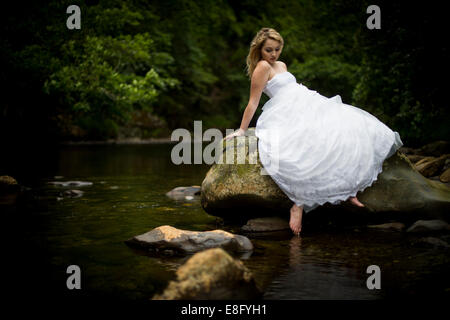 "Cestino il vestito": una giovane donna bionda ragazza modello 'sposa indossa un bianco Palla abito abiti da sposa immergendo la sua dita dei piedi nel fiume REGNO UNITO Foto Stock