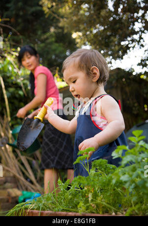 Un misto di etnia (East Asian / caucasica) toddler femmina nel piccolo giardino urbano a casa con la sua coreano East Asian madre Foto Stock