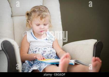 Adorabile bionda dai capelli blu Eyed Bambina leggendo il suo libro sulla sedia. Foto Stock