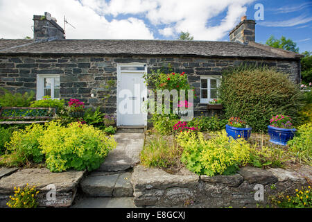 Piccolo cottage in pietra con parete di roccia, fasi e il percorso attraverso il colorato giardino al villaggio di Pitlochry, Scozia Foto Stock