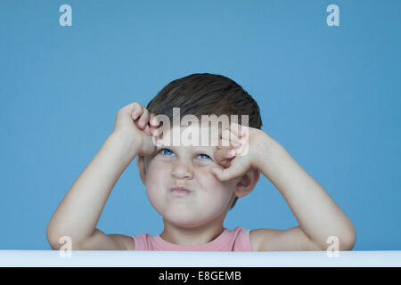 Tre anni giovane ragazzo tenendo le mani sul viso e express irritazione e rabbia emozione in posa sulla parete blu sullo sfondo Foto Stock