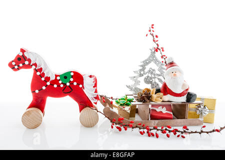 Babbo Natale seduto su rosso cavallo di legno sledge azienda dono e presenta - sfondo di Natale decorazione isolato Foto Stock