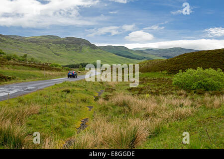 Paesaggio pittoresco con auto sulla strada stretta avvolgimento attraverso il verde delle colline, Heather e brughiere di highlands scozzesi Foto Stock