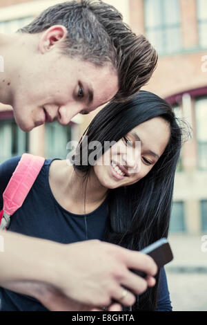 Gli studenti delle scuole superiori la lettura di un messaggio di testo sul telefono cellulare in schoolyard Foto Stock