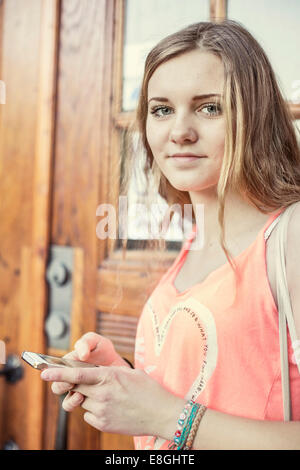 Ritratto di ragazza adolescente tramite telefono mobile in alta scuola schoolyard Foto Stock