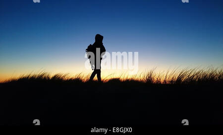 Silhouette di uomo a camminare nel paesaggio rurale al tramonto, Danimarca Foto Stock