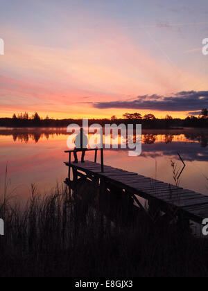 Silhouette di uomo seduto sul molo dal lago al tramonto, Gotaland, Svezia Foto Stock