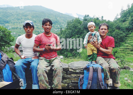 Tre uomini nepalesi seduti su un muro con un bambino, il Nepal Foto Stock