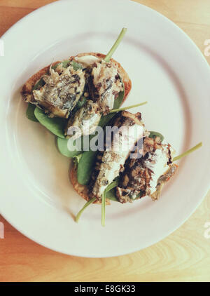 Sardine sul pane tostato con spinaci freschi verdi Foto Stock