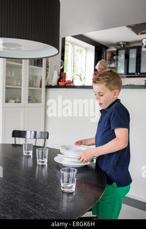 Ragazzo disponendo le piastre sulla tavola da pranzo a casa Foto Stock