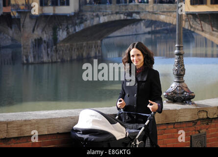 Madre spingendo una carrozzina vicino a Ponte Vecchio, Firenze, Toscana, Italia Foto Stock