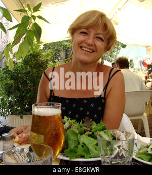 Donna seduta nel ristorante con insalata e birra Foto Stock