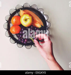 Donna raggiungendo a mano delle uve in coppa di frutta Foto Stock