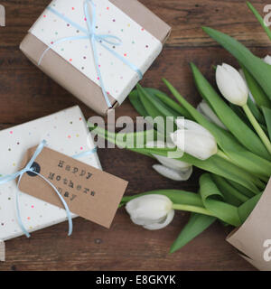 Vista dall'alto di un mazzo di tulipani bianchi e regali avvolti per la Festa della mamma su un tavolo Foto Stock