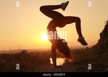 Giovane donna facendo handstand al tramonto Foto Stock