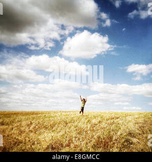 Ragazzo felice che corre attraverso un campo con le braccia in aria Foto Stock