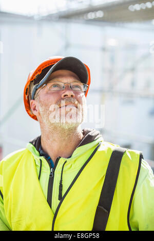 Operaio edile cercando mentre in piedi presso il sito Foto Stock