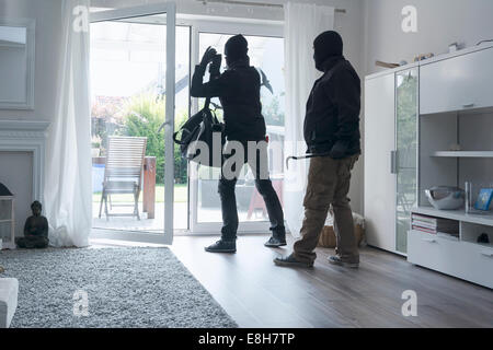 Due ladri lasciando una casa unifamiliare con il loro bottino di giorno Foto Stock