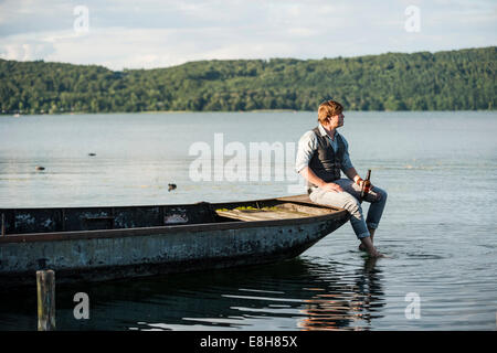 In Germania, in Renania Palatinato, Laach Lago, uomo con una birra seduti sulla barca a remi Foto Stock