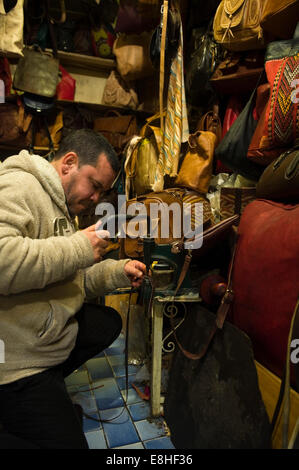 Ritratto verticale di un leatherworker fori di punzonatura in un cinturino in pelle di un negozio nel souk di Marrakech. Foto Stock