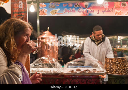 Ritratto orizzontale di un turista di bere il tè alla menta in una fase di stallo in Piazza Jemaa el Fna (Djemaa El Fnaa) in Marrakech di notte Foto Stock