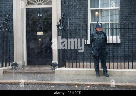 A Downing Street, Londra, Regno Unito. 08 ott 2014. Periodi di pioggia pesante ha colpito Londra oggi come il tempo è diventato autunnali positivamente. Nella foto: un poliziotto sta di guardia al di fuori 10 Downing Street durante una pioggia pesante. Credito: Lee Thomas/Alamy Live News Foto Stock