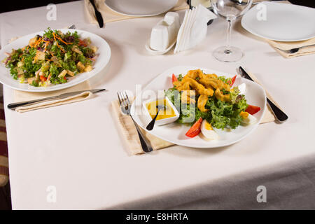 Gourmet pietanze salutari e gustose su bianco piastre tonde con utensili disposti su lati servita sul tavolo bianco per gli ospiti. Foto Stock