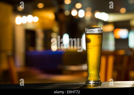 Bicchiere di birra sul bancone bar con sfondo sfocato Foto Stock