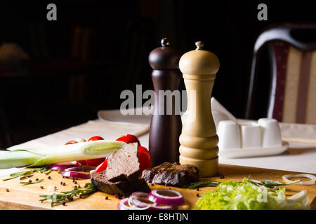 Sale e pepe Mills con affettato e tritate ingredienti pasto in ristorante tabella Foto Stock