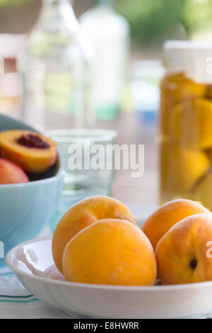 Picnic estivo di pesche gialle in un piatto con aqua bocce di nettarine e pesche conservate in background Foto Stock