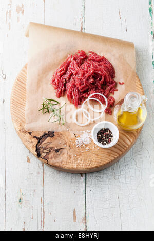 Freschi di carne macinata con cipolla e spezie sul tagliere di legno su sfondo blu Foto Stock