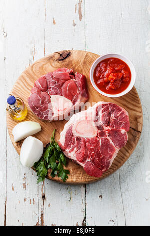 Materie carni fresche bovine stinchi per la produzione di Osso Buco sul tagliere di legno sul blu sullo sfondo di legno Foto Stock