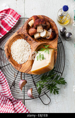 Materie riso in bianco in legno d'olivo ciotola con ingredienti per il risotto con funghi selvatici Foto Stock