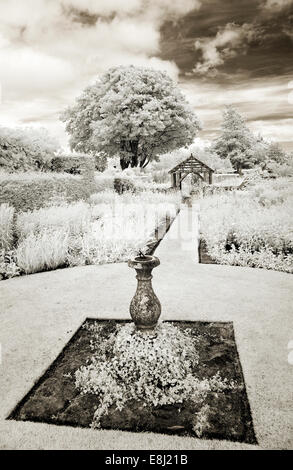 Fotografia a infrarossi di un classico giardino inglese meridiana ornata funzione sul prato con bordi di piante erbacee perenni a Wollerto Foto Stock