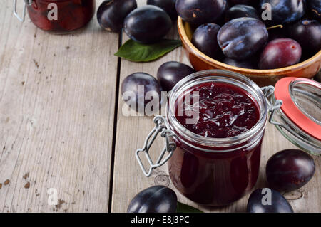 In casa di marmellata di prugne e gruppo di prugne sul vecchio tavolo in legno. Abbondanza di copyspace. Foto Stock