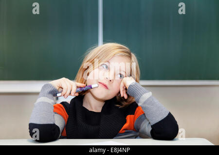 La scolaretta, 9 anni, pensieroso, seduto di fronte a una lavagna Foto Stock