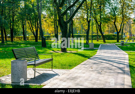 Panca vicino al percorso del cemento in un tranquillo parco della città inizio autunno in una giornata di sole Foto Stock