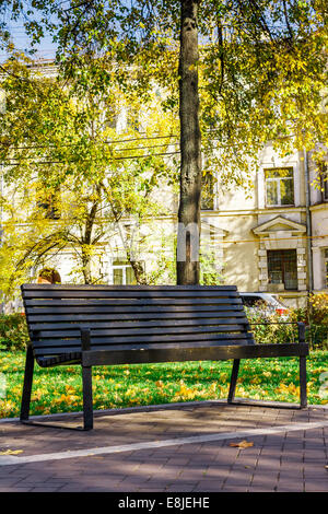 Lonely brown panca di legno in un tranquillo parco della città sullo sfondo di una vecchia casa in inizio di caduta in una giornata di sole Foto Stock