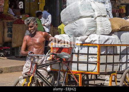 In rickshaw driver e il suo peso di un carico molto pesante in India Foto Stock