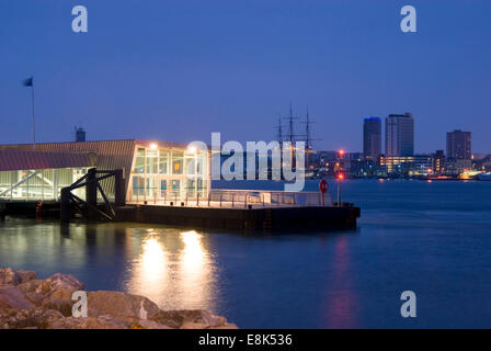 Gosport e il porto di Portsmouth, Regno Unito 07 aprile 2013: Gosport Ferry Jetty illuminata di notte con HMS Warrior attraverso il porto di Portsmouth Foto Stock