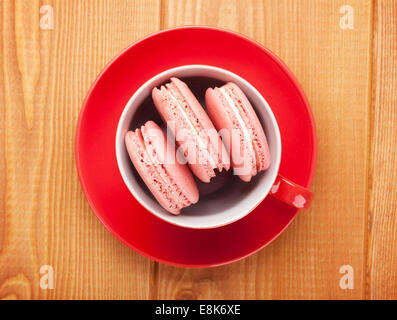 Rosa macaron i cookie nella tazza di caffè sul tavolo in legno sfondo Foto Stock