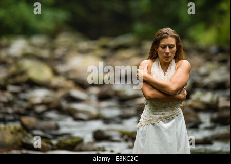 Cestino il vestito: un "sposa' che indossa il suo abito da sposa in piedi in riverbed cercando freddo brividi introverso da soli con le braccia incrociate Foto Stock