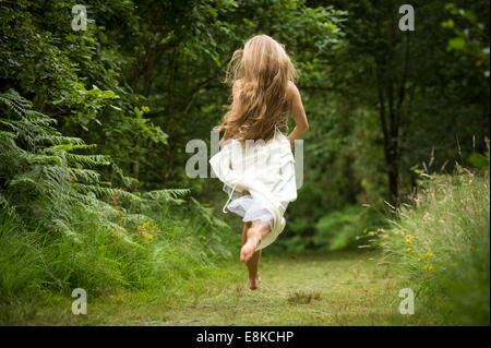 Runaway bride, vista posteriore di un sottile caucasici sani giovane donna ragazza con lunghi capelli biondi di scappare su un percorso nel bosco foresta bianca che indossa abiti da sposa tonaca in campagna REGNO UNITO Foto Stock